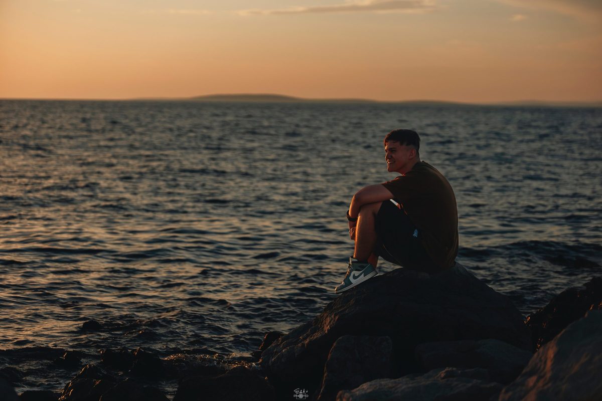 Rizmajer Máté Levente naplementében, egy sziklán ülve